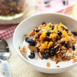 A healthy bowl of yogurt topped with granola and oranges.