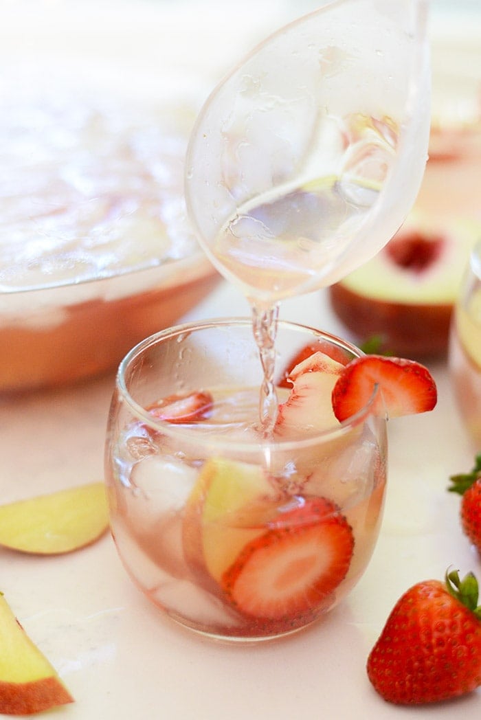 Strawberry Peach Rosé Sangria being poured into a stemless wine glass