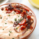 A bowl of roasted red pepper and goat cheese dip with onions and tomatoes.