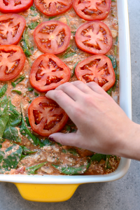 a person is removing tomatoes from a Naked Spinach Quinoa Lasagna Casserole.