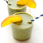Two glasses of green smoothie with orange slices.