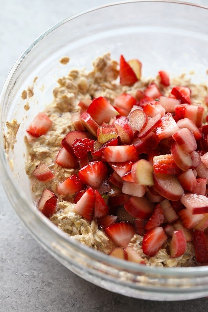 Bowl of sliced strawberries and rhubarb with oatmeal ready to be stirred and placed in a baking dish.