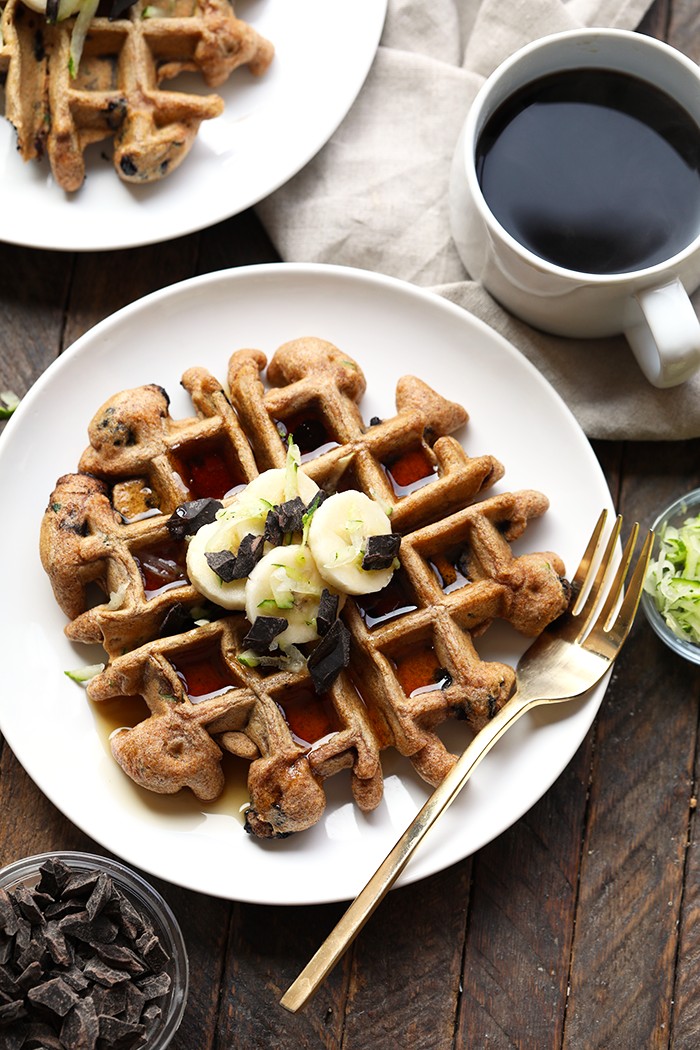 You will absolutely love this zucchini waffle recipe because it's made with whole wheat flour, shredded zucchini, coconut oil, and real maple syrup. zucchini waffles with bananas on plate.