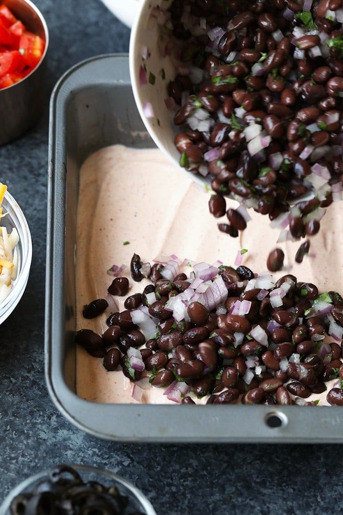 black bean layer of taco dip being poured into a pan