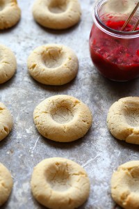 A tray of Raspberry Thumbprint Cookies on a baking sheet with a jar of jam.
