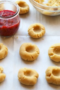 Raspberry Thumbprint Cookies on a baking sheet with a bowl of jam.