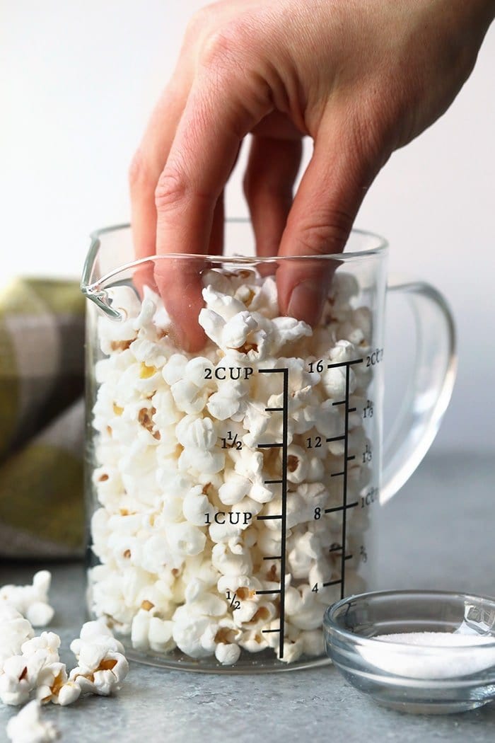 Make snack time easy and healthy tonight with our stovetop popcorn tutorial. In under 10 minutes, this low-calorie snack is popped and ready to go hand reaching for popcorn in glass