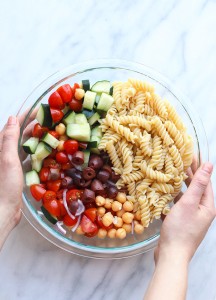 A person holding a bowl of Greek pasta salad.