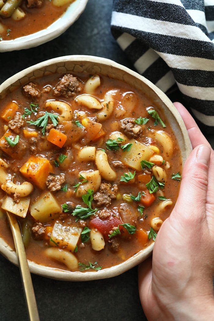This Instant Pot Hamburger Soup recipe is a healthy weeknight meal that everyone will love! It is packed with protein, vegetables, and is ready in less than an hour. A hand holding a bowl of hamburger soup