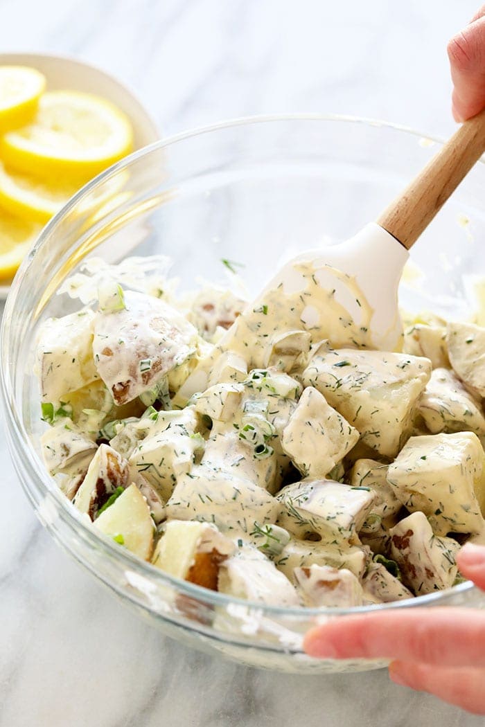 This vegan potato salad is light, bright, and delicious! Not only is this potato salad the perfect summer side, but it's also so easy to make. A hand mixing vegan potato salad in a bowl.