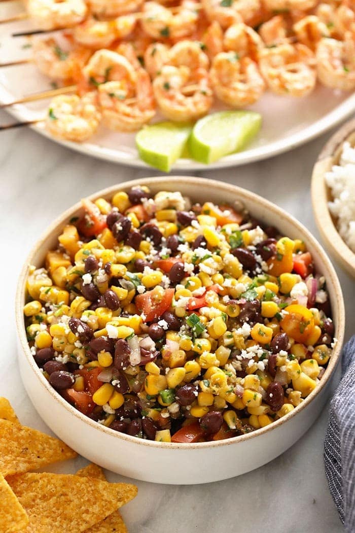 Black bean corn salad with grilled shrimp on skewers in the background.