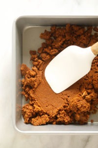 a white spatula is being used to mix the ingredients for pumpkin cheesecake bars in a baking pan.