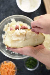 A person slices a potato with a knife to prepare twice baked potatoes.