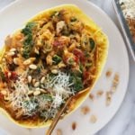 Instant Pot spaghetti squash boats with spinach and pine nuts on a white plate.