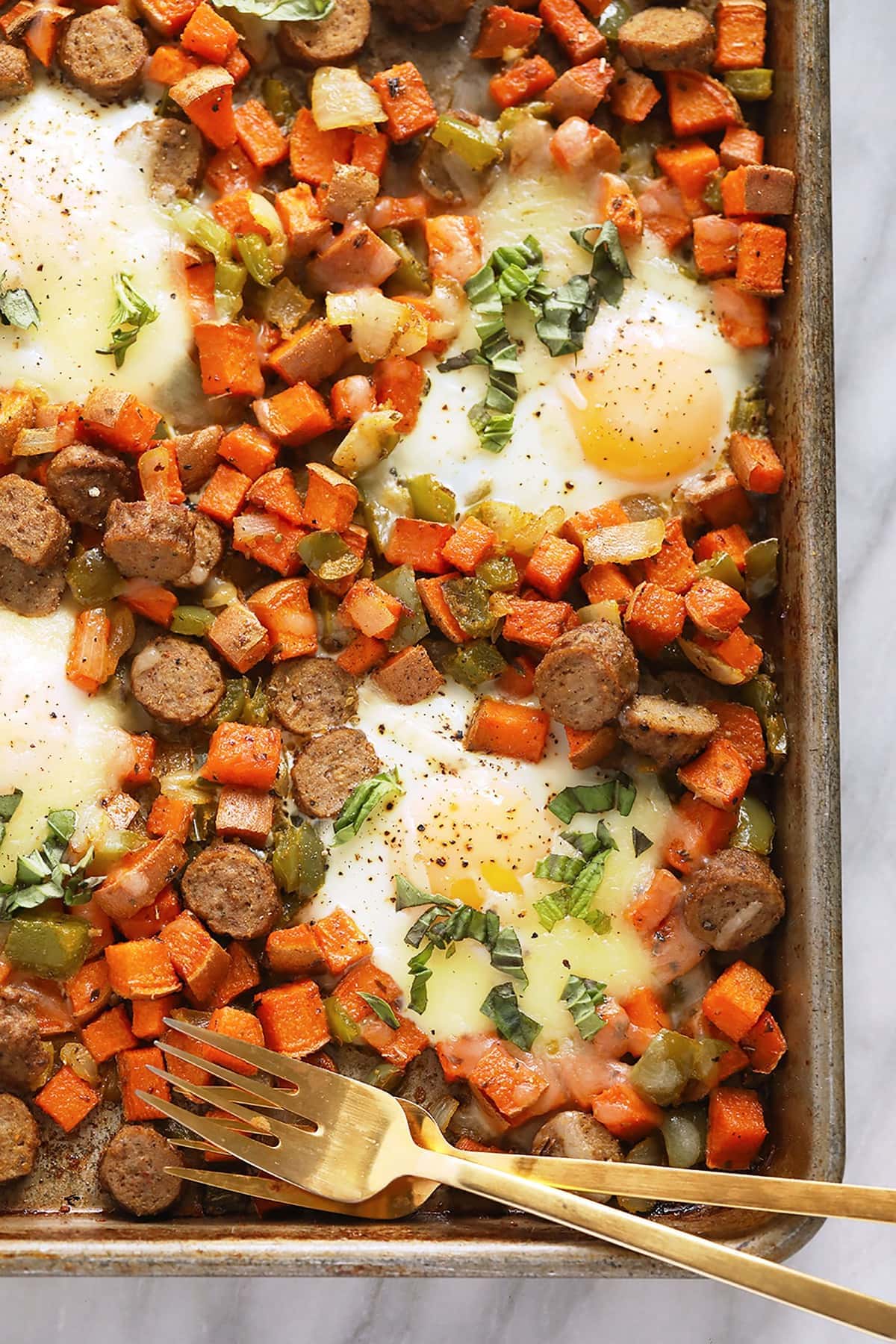 With just one sheet pan you can whip up the most delicious and nutritious sweet potato hash using pantry staple ingredients! sweet potato hash on baking sheet with eggs and 2 forks.
