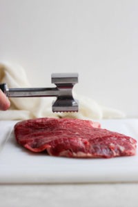 tenderizing flank steak on cutting board.