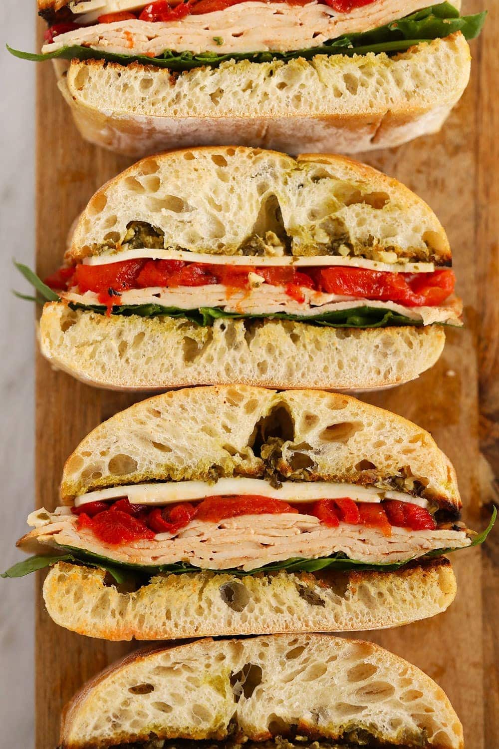 Forget the subway party platter and make this Grilled Roasted Red Pepper, Pesto, & Turkey sandwich! It is perfectly toasted on the grill and a great meal for the family or a larger group at a bbq! Grilled Roasted Red Pepper, Pesto & Turkey Sandwich on a cutting board