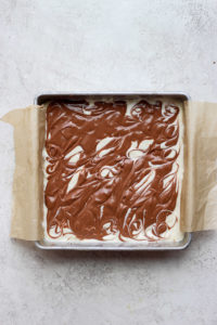 Cheesecake bars with chocolate icing in a baking pan.