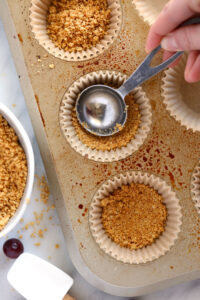 a person pouring granola into a muffin tin.