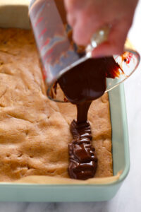 a person drizzling chocolate over a peanut butter protein bar in a pan.