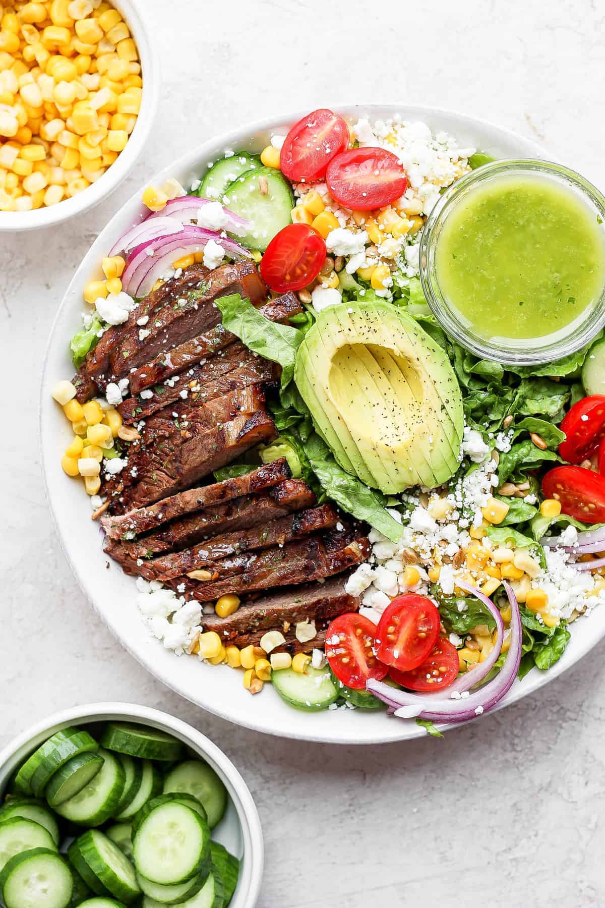 The tastiest steak salad recipe that uses beautifully grilled steak, tons of veggies, goat cheese, avocado, and an herby dressing. steak salad in bowl with dressing.