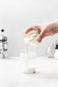 a hand pouring milk into a glass jar.