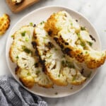 a white plate topped with cauliflower next to a cutting board.