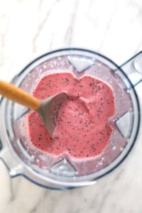 a blender filled with a pink smoothie with a wooden spoon.