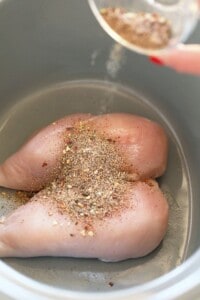 A person is seasoning and slow cooking chicken in a slow cooker for pulled chicken.