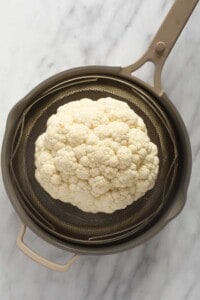 a head of cauliflower in a strainer.