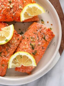 grilled salmon on a white plate with lemon wedges.