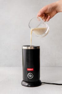 A person preparing a London Fog drink by pouring milk into a coffee maker.
