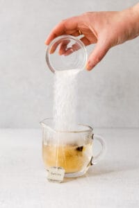 a hand is pouring sugar into a cup of London fog tea.