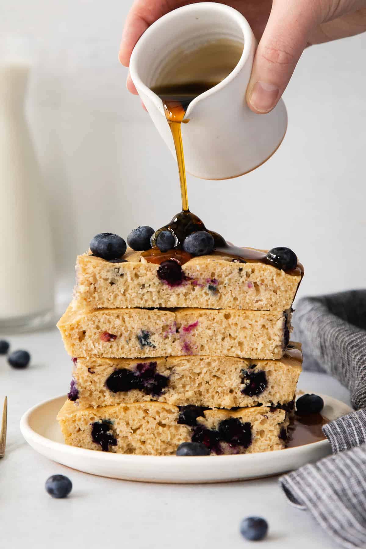 Take the ease out of making pancakes with this Sheet Pan Pancakes recipe. Instead of pour, flip, and repeat, bake your pancake batter in a sheet pan for a hands-off breakfast that serves a crowd! pouring syrup on pancakes