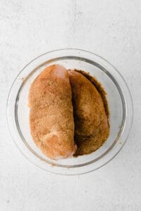 two pieces of chicken in a glass bowl on a white surface.