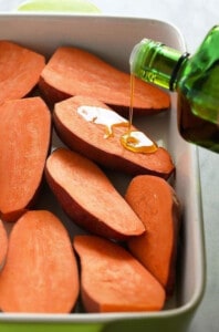 Sweet potatoes bring drizzled with olive oil in a baking dish.