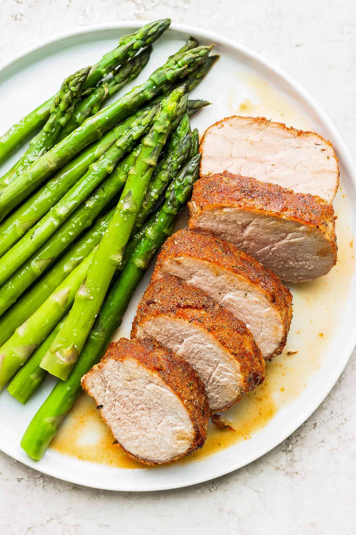 This Air Fryer Pork Tenderloin recipe is super moist on the inside with a crispy outside and is ready to enjoy in minutes. air fryer pork tenderloin on a plate with asparagus