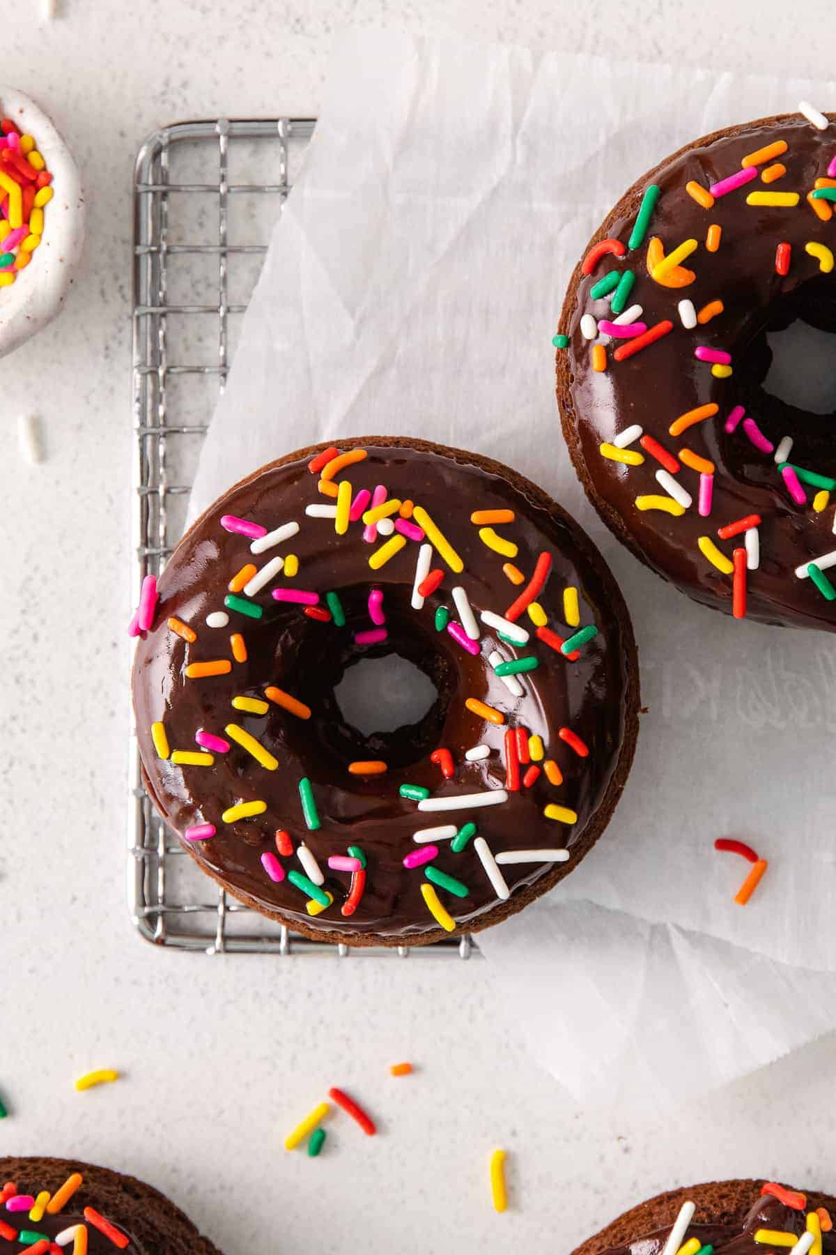 These tender chocolate baked donuts are baked in the oven and never fried. They're perfectly tender and topped with a yummy chocolate frosting and sprinkles. donut on wire rack