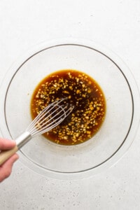 A person whisking an asian sauce in a glass bowl.