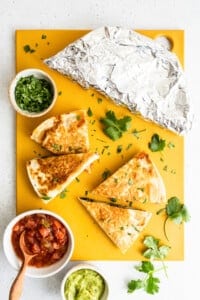 Quesadillas and guacamole on a yellow cutting board.