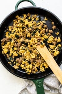 Scrambled eggs in a skillet with a wooden spatula.