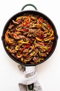 Beef enchilada in a skillet with peppers and onions.