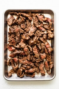 Beef in a metal pan on a white surface.