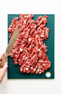 A person cutting a piece of beef on a cutting board.