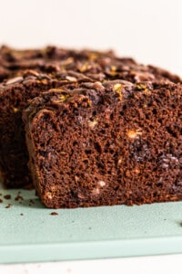 A slice of chocolate zucchini bread on a green cutting board.