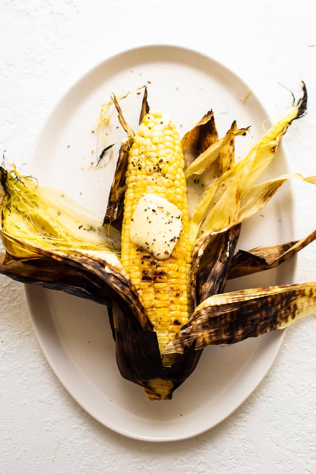 Corn on the cob on the grill is an easy summer side to make that only requires a few ingredients. Learn how to grill corn on the cob in the husk and without it! grilled corn on a plate with butter.
