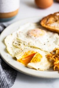 A plate with a fried egg, potatoes and a jar of peanut butter.