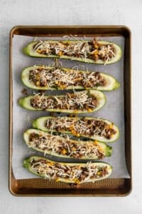 Zucchini boats with meat and cheese on a baking sheet.