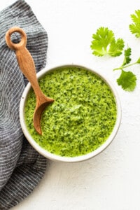 A bowl of green sauce with a wooden spoon.