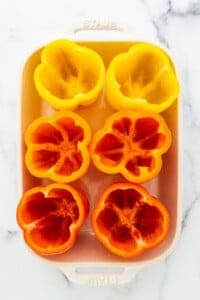 Sliced red and yellow peppers in a white baking dish.